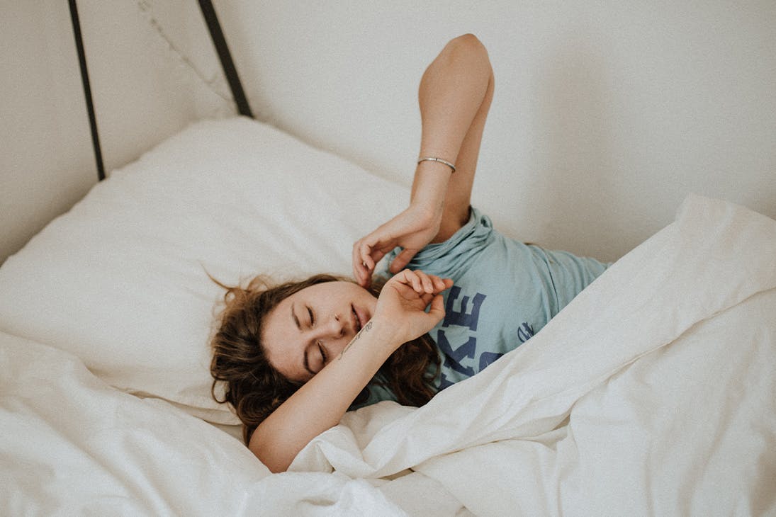 woman wearing a blue shirt lying bed alone with her eyes closed